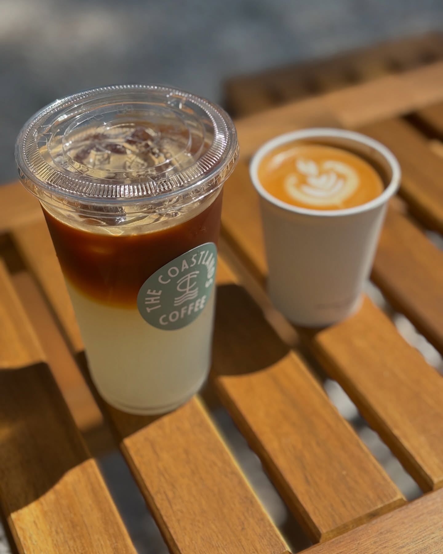 An iced coffee and hot latte on a sunlit wooden table.